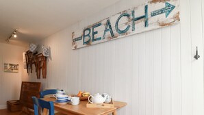 Un área de comedor con una mesa de madera, sillas azules y un letrero en la pared que dice "BEACH".