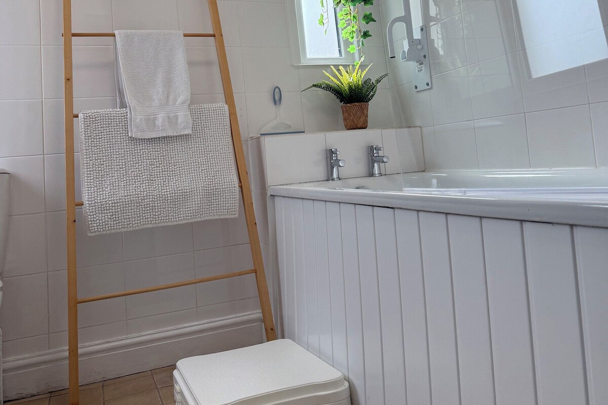 A bathroom with a wooden ladder, a white bathtub, a sink, and a potted plant.