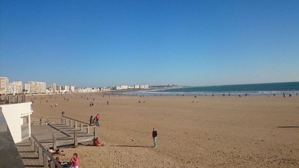 Una playa extensa con un paseo marítimo de madera y edificios al fondo.