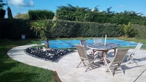 Un patio con una mesa redonda y sillas, una palmera pequeña y una piscina.