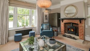 A living room with a fireplace, a blue sofa, a glass coffee table, and a chandelier. - The Gate House (Cirencester)