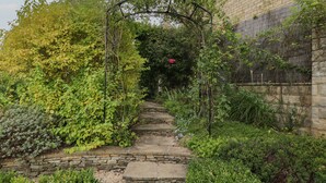 A stone pathway leading through a lush garden with a brick wall on one side and a wooden fence on the other. - The Gate House (Cirencester)