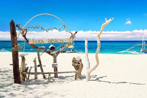 A beach sign labeled "PUKA BEACH" with a donation box, surrounded by driftwood and a clear blue sky. - Grospe Resort Boracay (Boracay Island)