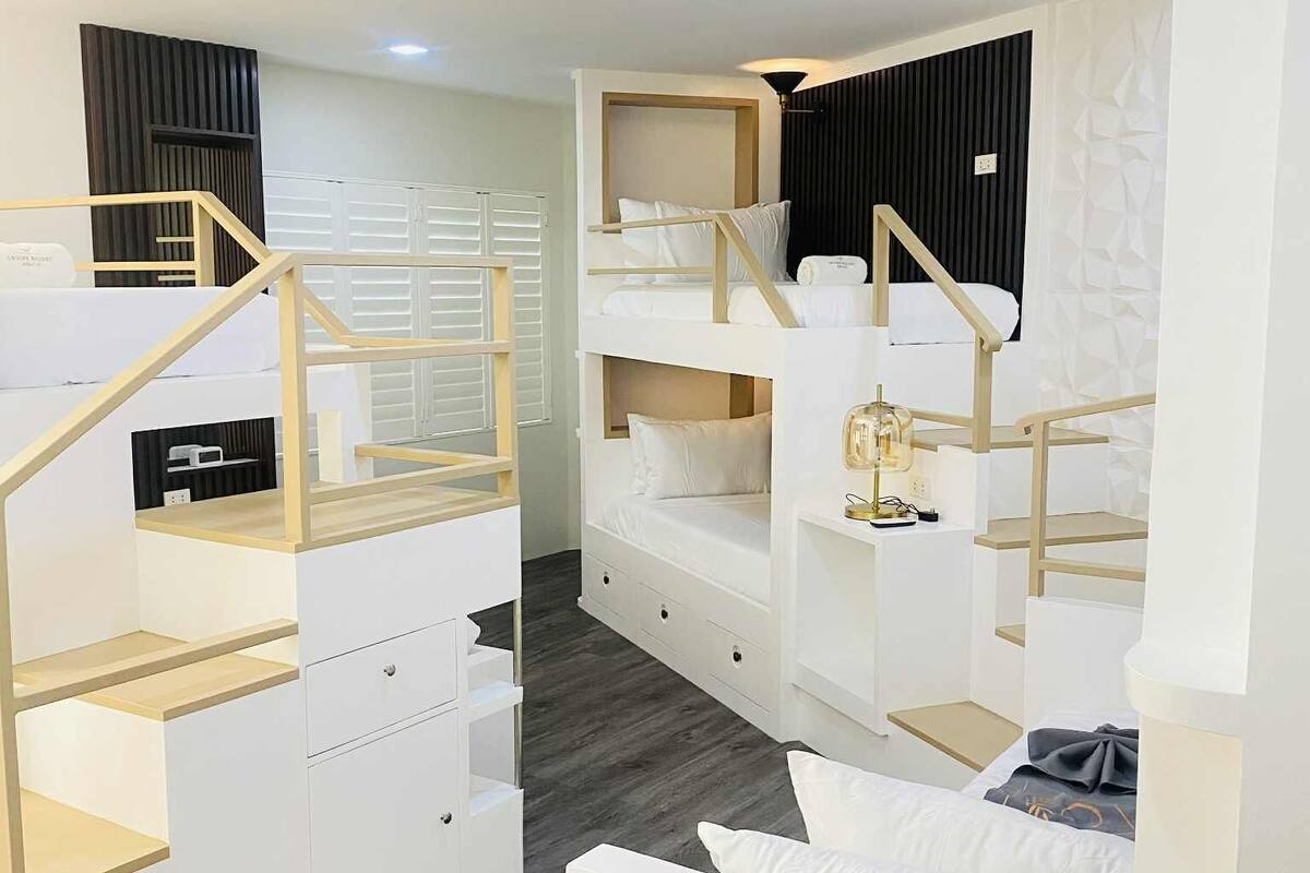 Une chambre compacte et moderne, dotée de lits superposés et de rangements intégrés, avec un escalier en bois et un petit espace bureau.
