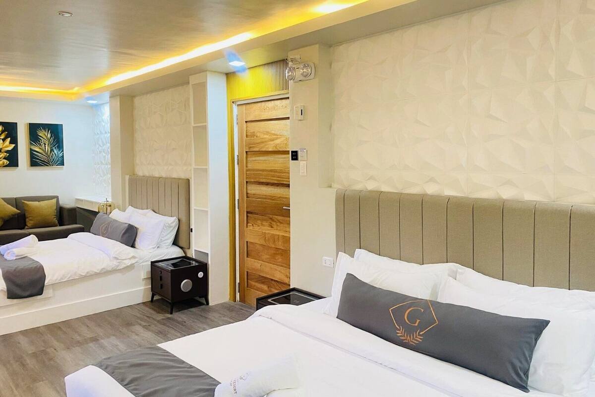 Une chambre d’hôtel avec deux lits, un canapé, une petite table et une armoire en bois.