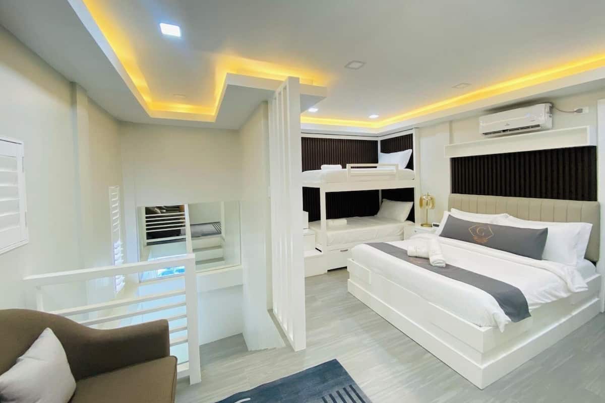 Une chambre d’hôtel moderne équipée d’un lit superposé, d’un lit séparé, d’un canapé et d’un balcon avec une rambarde.