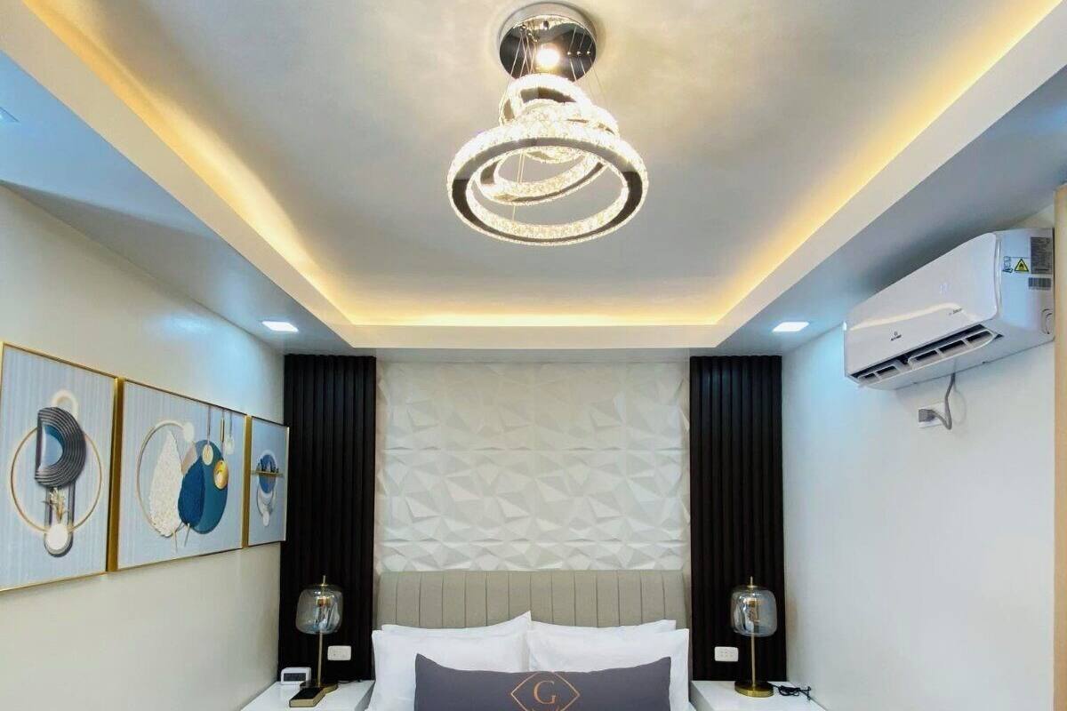 Une chambre d’hôtel moderne, dotée d’un grand lit, d’un luminaire au plafond, d’un appareil de climatisation et d’œuvres d’art accrochées aux murs.