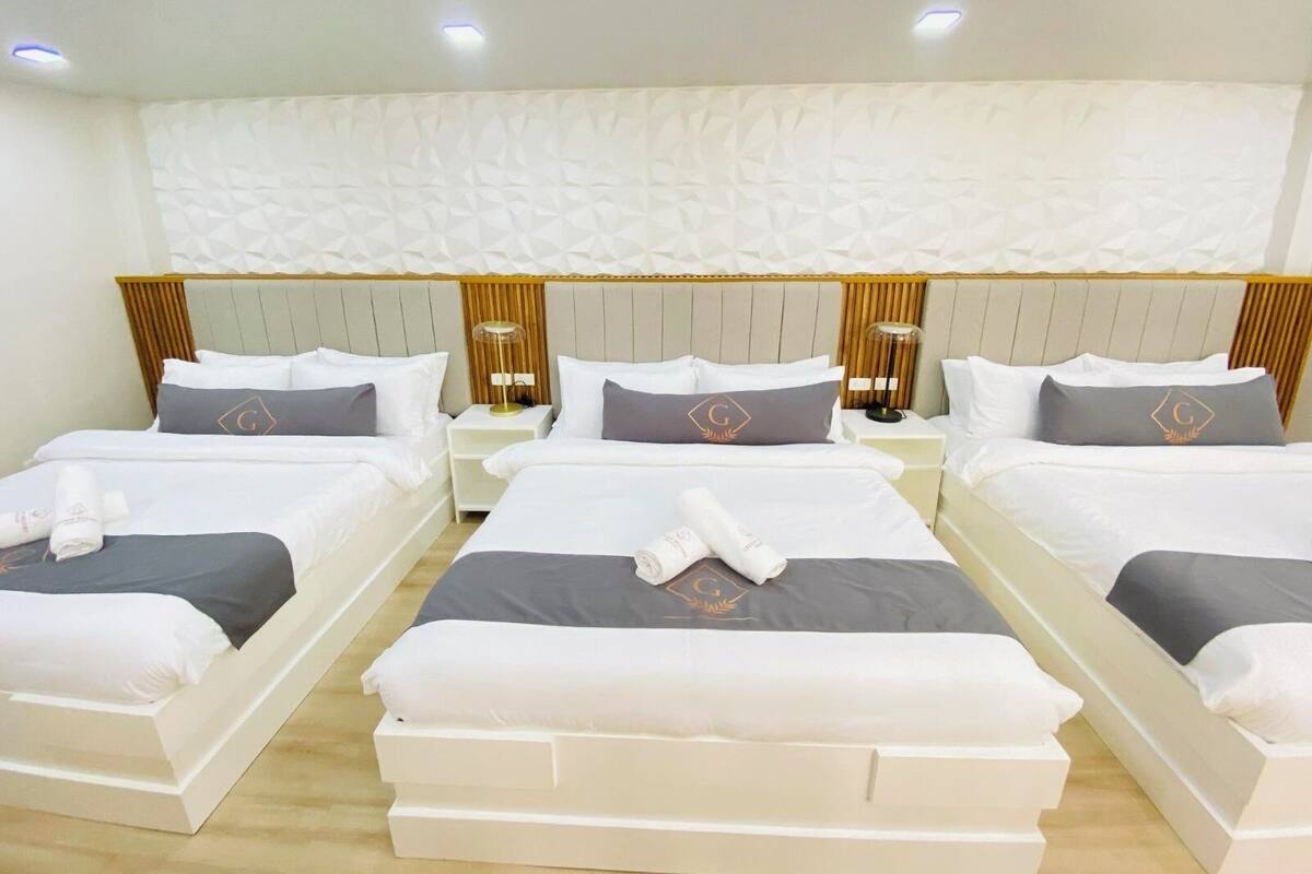 Une chambre d’hôtel avec quatre lits alignés, chacun étant doté de draps blancs et d’oreillers gris.