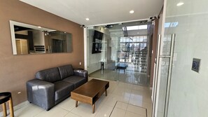 Relax in this stylish living room with a sofa, coffee table, and large mirror, offering a view of the surrounding area through the glass door.