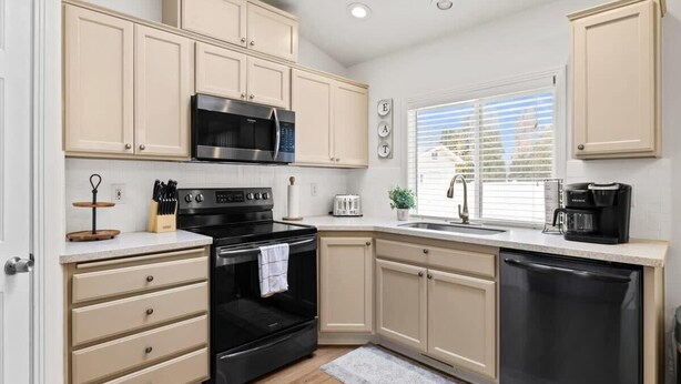 Une cuisine moderne avec des meubles de couleur beige, une cuisinière noire, un four à micro-ondes, un lave-vaisselle et une fenêtre équipée de stores.