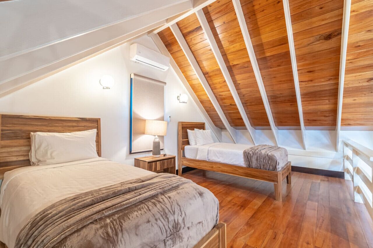 Ein Schlafzimmer mit zwei Betten, Holzbalkendecke, einem Nachttisch mit Lampe und einem Fenster.
