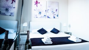 Quarto de hotel com uma cama, duas mesas de cabeceira, uma mesinha de apoio, uma janela com cortinas e obras de arte nas paredes.