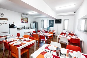 A modern dining area with tables and chairs, a clock, an air conditioning unit, and a television on the wall. - DOMUS in PANTHEON (Rome)