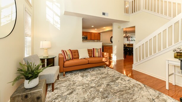 A spacious living room with a large sofa, a coffee table, and a rug. There is a staircase leading to an upper level.