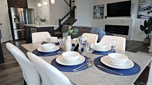 Ein moderner Essbereich mit gedecktem Tisch, weißen Stühlen und einer Küche im Hintergrund.