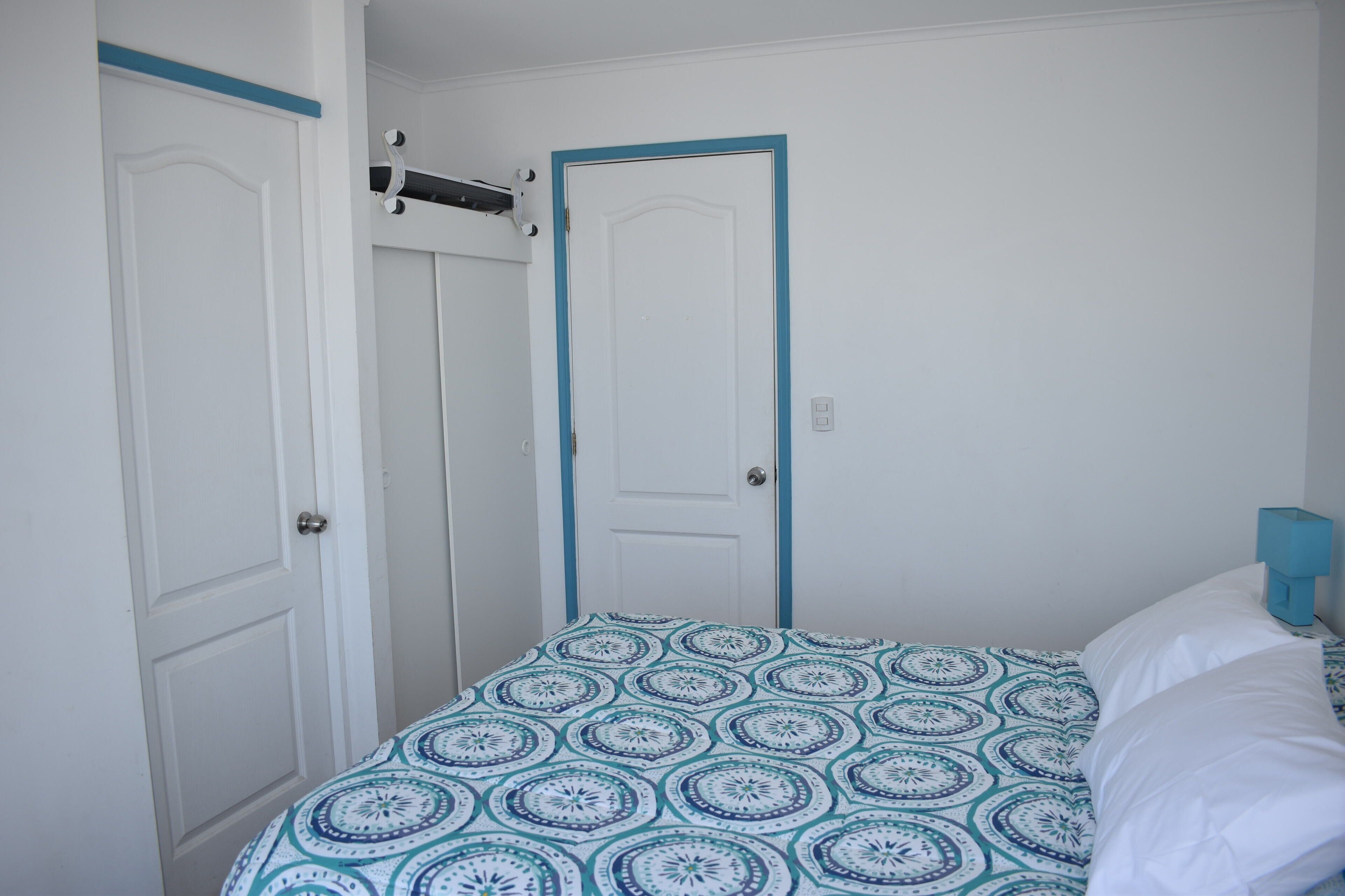 Un dormitorio con cama, puerta y estante fijado a la pared.