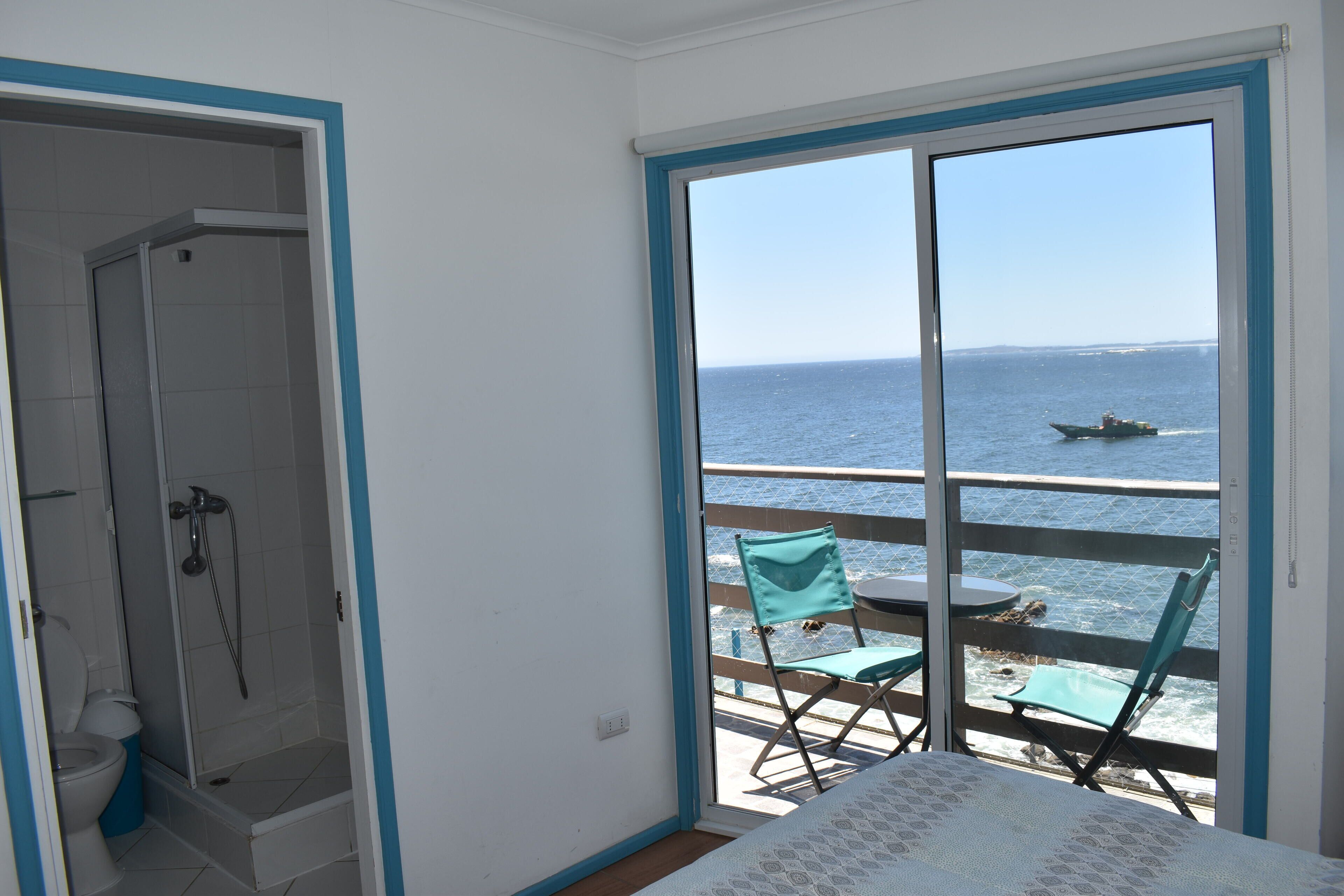 A balcony with a view of the sea, a small table, and a chair.