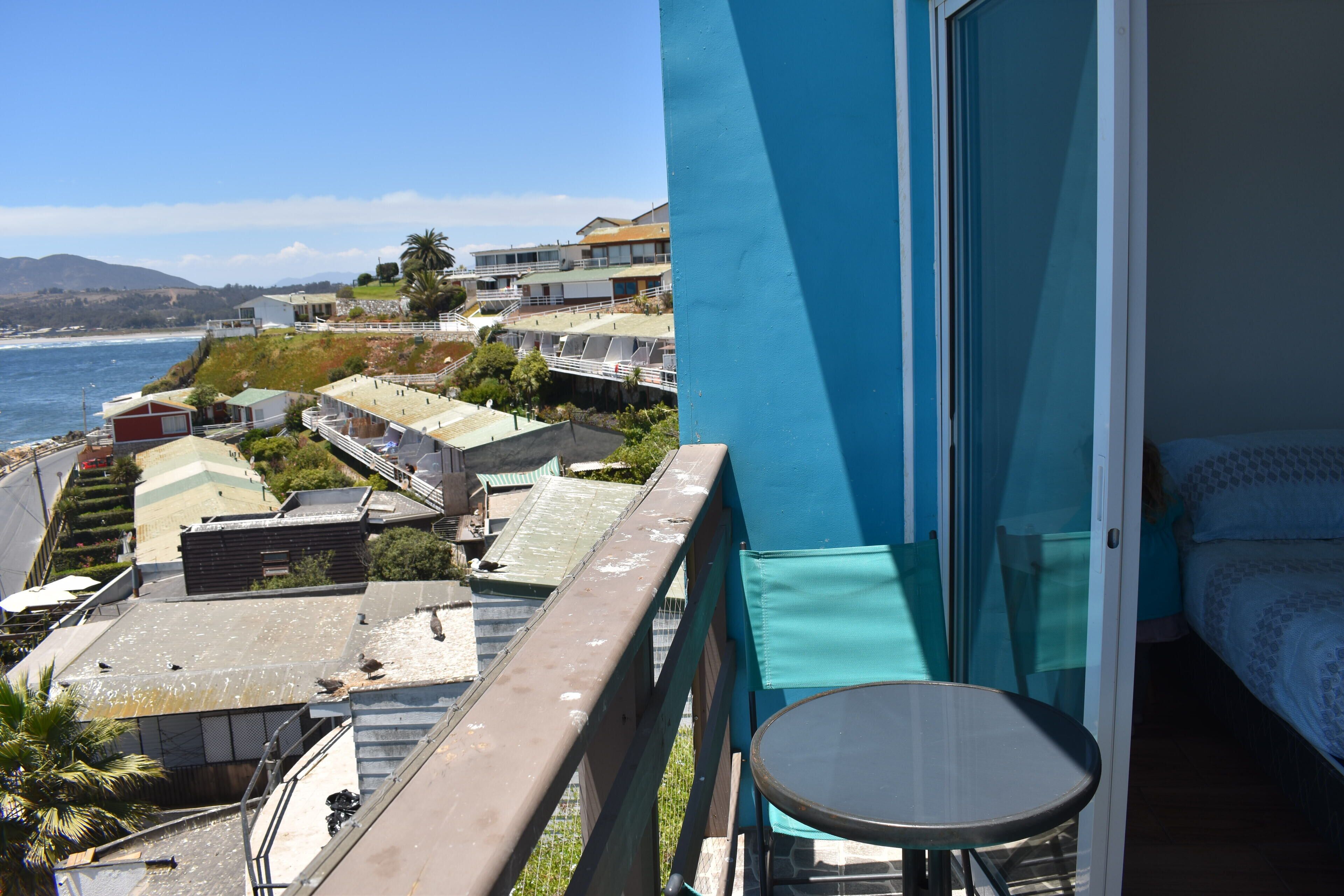 A balcony with a view of the ocean and hillside buildings.