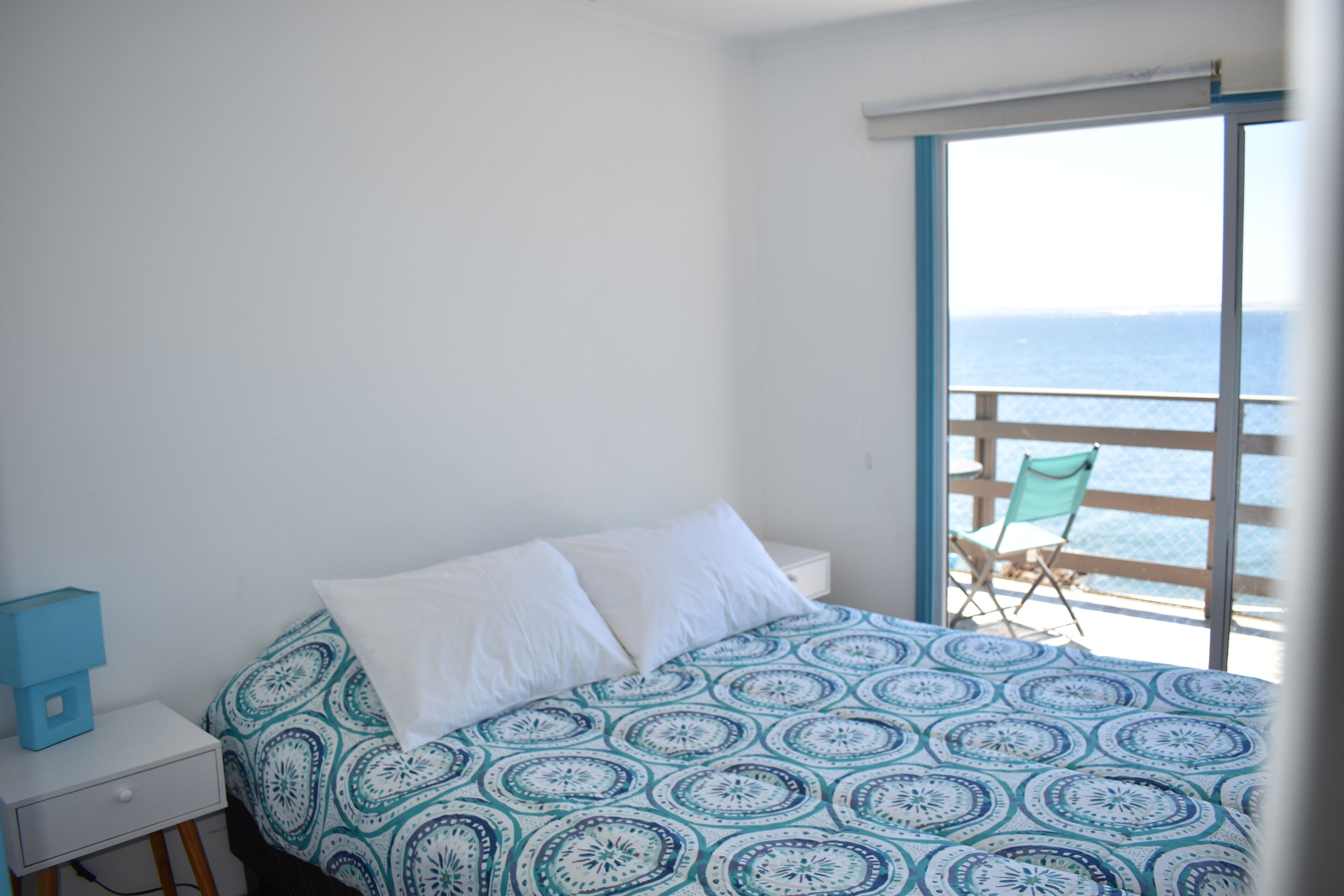 A bedroom with a bed, a nightstand, and a view of the sea through a balcony door.