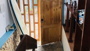 Una puerta de madera con un ventanal, una tabla de surf apoyada en la pared y una escalera que conduce a un suelo de piedra.