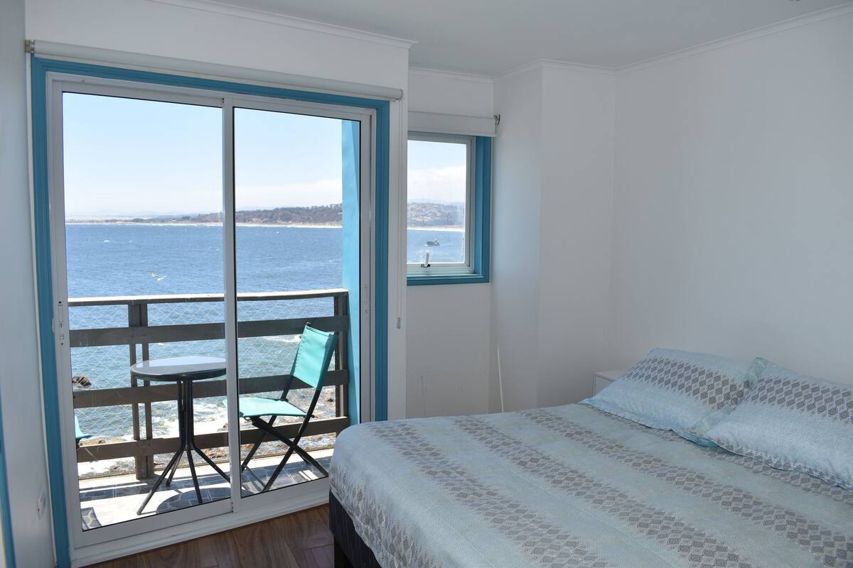 A bedroom with a bed, a window, and a view of the sea.
