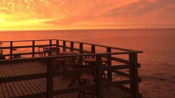 A wooden deck with tables and chairs overlooking the ocean at sunset.