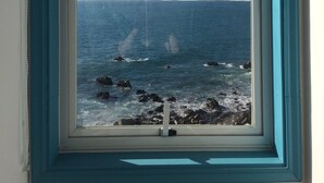 Una ventana con vista al océano y a la costa rocosa.
