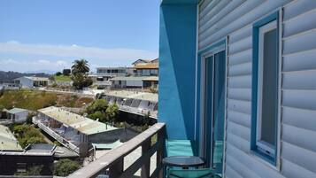 Un balcón con vistas a la costa, incluyendo un edificio con revestimiento azul y una palmera.