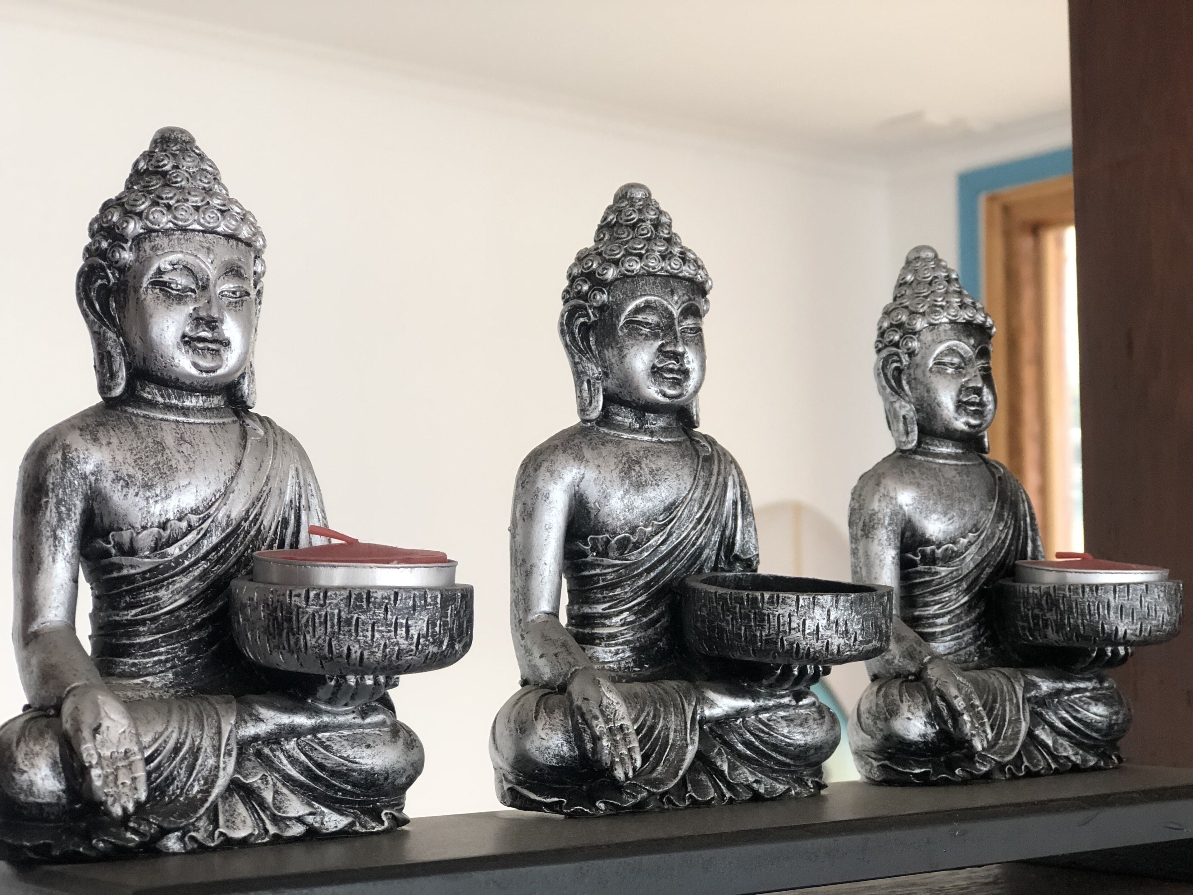 Tres estatuas metálicas de Buda sentadas sobre una repisa.