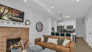 A modern living room with a fireplace, a sofa, ottomans, and a television mounted on the wall. - 3BD West Town Gem: Explore the Windy City in Style (Chicago)