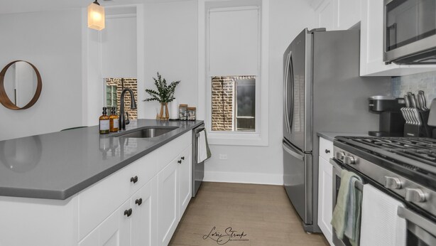A modern kitchen with white cabinetry, a stainless steel refrigerator, a stove, and a large island with a light fixture above. - 3BD West Town Gem: Explore the Windy City in Style (Chicago)