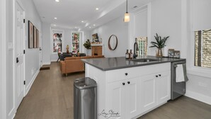 A modern kitchen with white cabinetry, a central island, and a dining area with a brown sofa. - 3BD West Town Gem: Explore the Windy City in Style (Chicago)