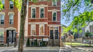 A multi-story brick building with a black metal fence, a tree in front, and a clear sky. - 3BD West Town Gem: Explore the Windy City in Style (Chicago)