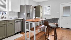 A modern kitchen with white cabinets, a stainless steel refrigerator, a wooden dining table, and a bar stool. - SWEET HOUSTON 14 people, 4 Bethrooms, 2 Full Bath. Pool, Central Houston. (Houston)