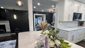 A modern kitchen with white cabinets, a marble countertop, and a dining area with a table set for two. - Casa 22 Luxury & Modern 3BD 2BA Home in Skokie (Skokie)