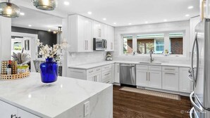 A modern kitchen with white cabinetry, a stainless steel refrigerator, and a blue vase on the island. - Casa 22 Luxury & Modern 3BD 2BA Home in Skokie (Skokie)