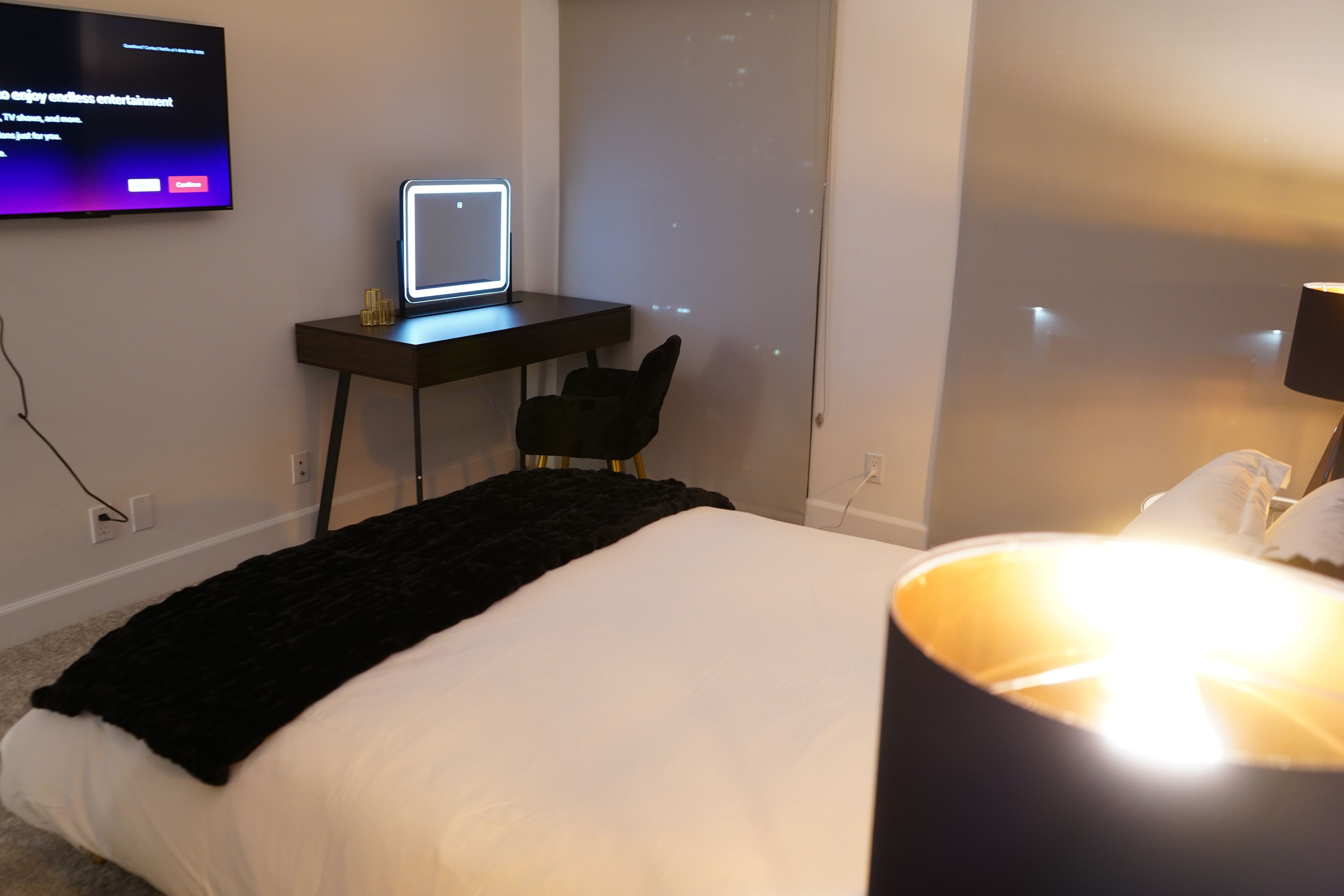 Une chambre d’hôtel avec un lit, un bureau équipé d’un ordinateur, un téléviseur fixé au mur et une lampe.