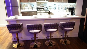 Une cuisine moderne dotée d’un îlot central, d’appareils électroménagers en acier inoxydable et de quatre tabourets de bar.