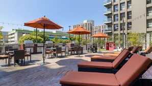 Un bar situé sur le toit, avec des fauteuils confortables et des parasols, une terrasse en briques et une vue sur un bâtiment moderne en arrière-plan.