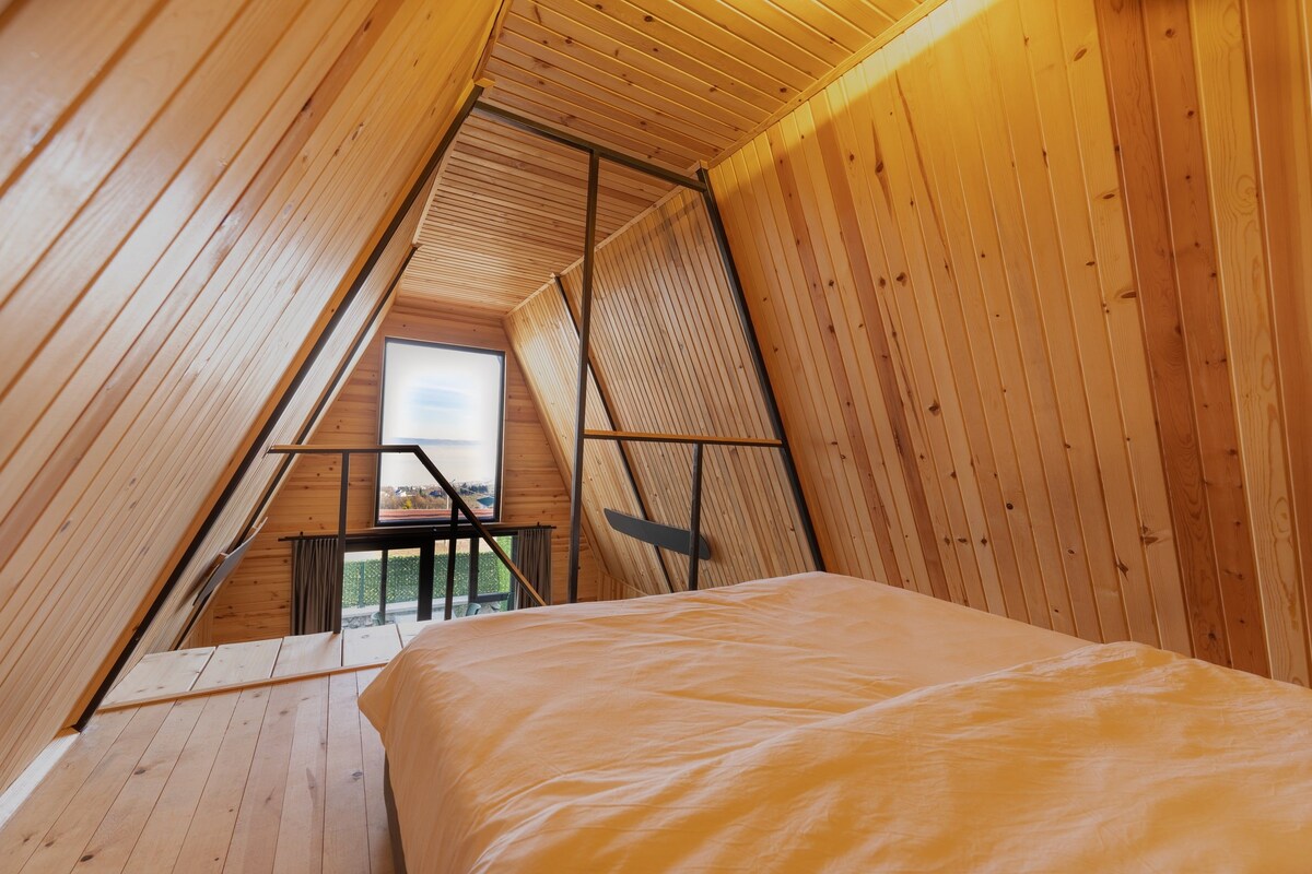 A high-ceilinged wooden room with a bed, a table, and a view through a window.