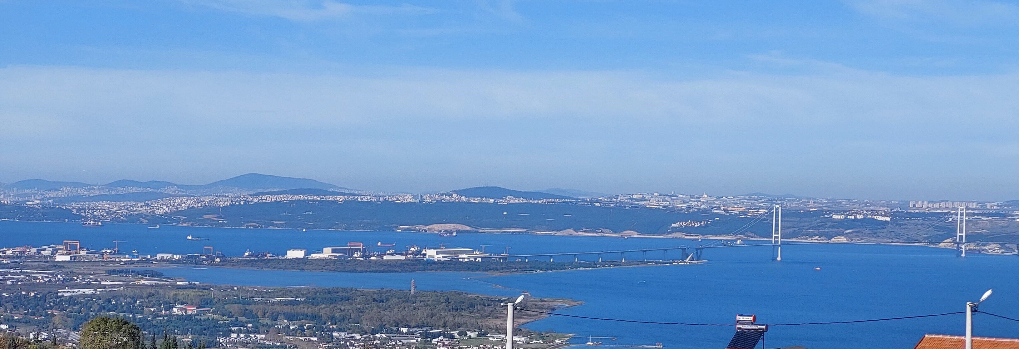 Un paisaje urbano costero con un puente destacado, edificios industriales y un fondo montañoso.