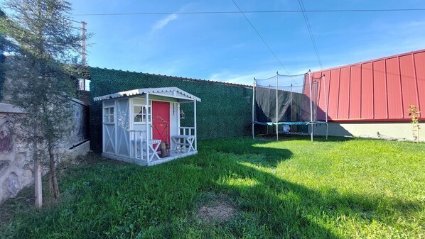 Un área de juegos pequeña, cercada, con una puerta roja y un edificio blanco con porche.