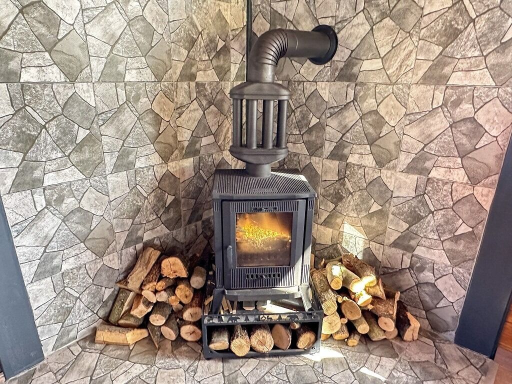 A wood-burning stove with logs in front, set against a mosaic tile wall.