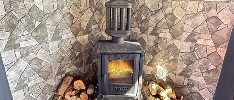 A wood-burning stove with logs in front, set against a mosaic tile wall.