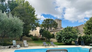 Piscina com espreguiçadeiras, rodeada por vegetação e um edifício de pedra ao fundo.