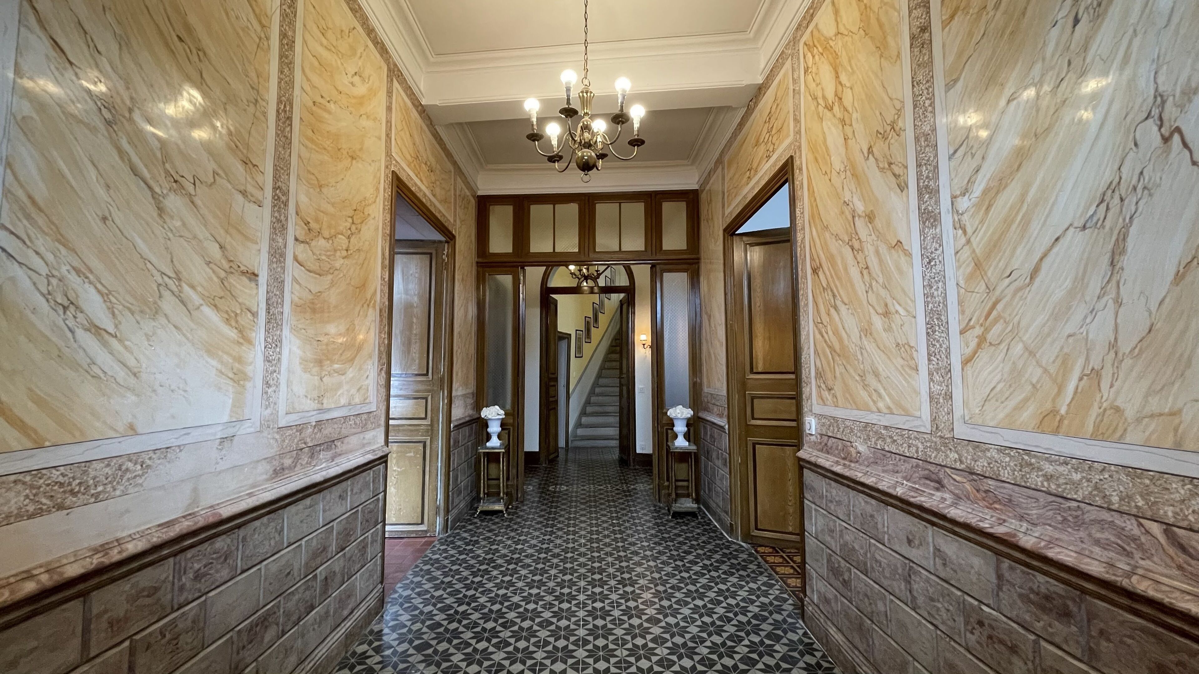 A hallway with marble walls, a patterned floor, and a chandelier.