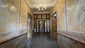 Um corredor com paredes de mármore, piso estampado e um candelabro.