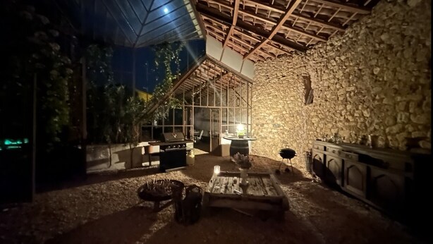 Um pátio externo com paredes de pedra, churrasqueira e mesa com cadeiras.