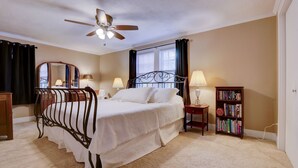 Une chambre à coucher comprenant un lit, un ventilateur de plafond, une table de chevet avec une lampe, une bibliothèque et une fenêtre avec des rideaux.