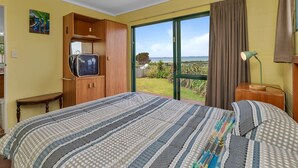 Un dormitorio con cama, armario de madera, televisor, mesa y vista al exterior.